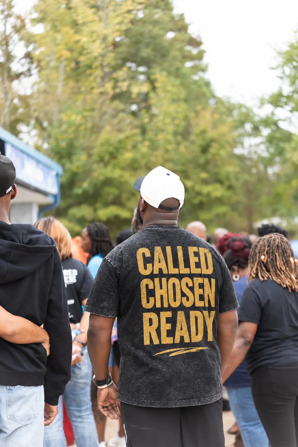 A Kingdom Agency team member seen from behind wearing a CALLED. CHOSEN. READY. shirt at an outdoor gathering